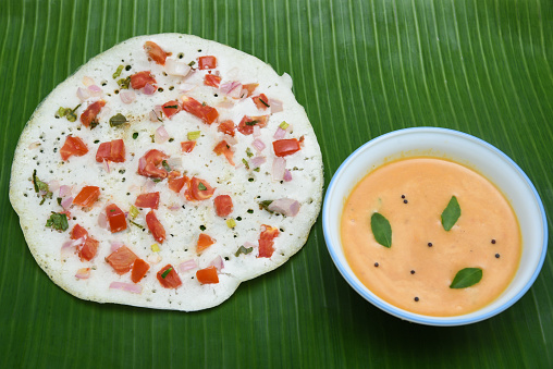 South Indian breakfast Oothappam / Dosa cooked using rice lentil and vegetables served with coconut chutney and sambhar isolated on black. popular dish in Kerala and Tamil Nadu India.