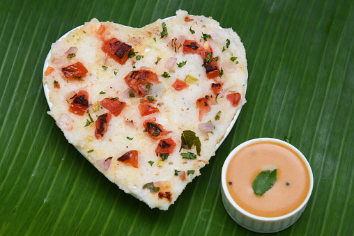 South Indian breakfast Oothappam / Dosa cooked using rice lentil and vegetables served with coconut chutney and sambhar isolated on black. popular dish in Kerala and Tamil Nadu India.