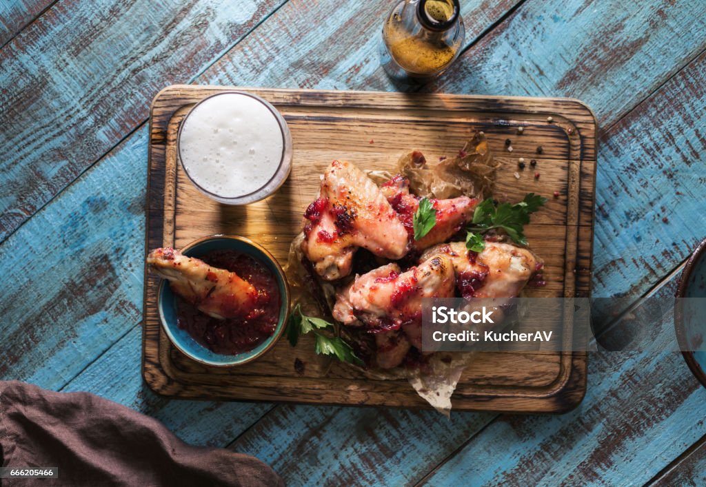 Chicken wings in cranberry sauce served on a wooden board with a glass of light beer Chicken wings in cranberry sauce served on a wooden board with a glass of light beer, top view Chicken Wing Stock Photo