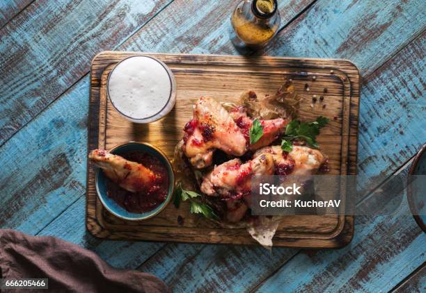 Chicken Wings In Cranberry Sauce Served On A Wooden Board With A Glass Of Light Beer Stock Photo - Download Image Now