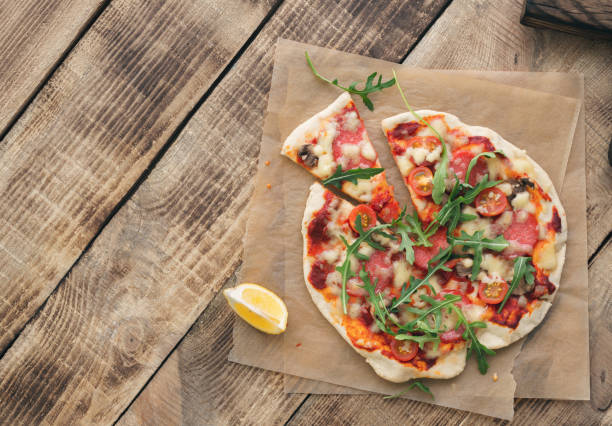 Italian pizza with salami, cherry tomato, mushrooms and arugula on wooden table Italian pizza with salami, cherry tomato, mushrooms and arugula on wooden table with copy space tortilla flatbread stock pictures, royalty-free photos & images