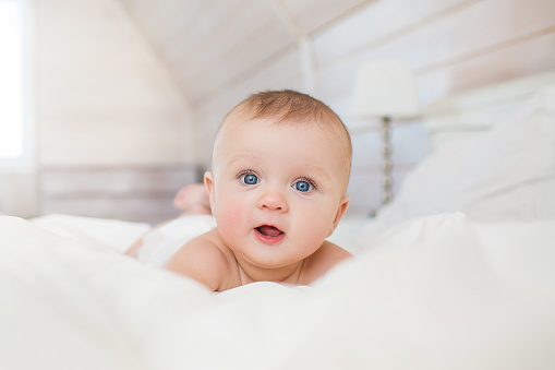 Portrait of little infant lies on a white bed in bedroom