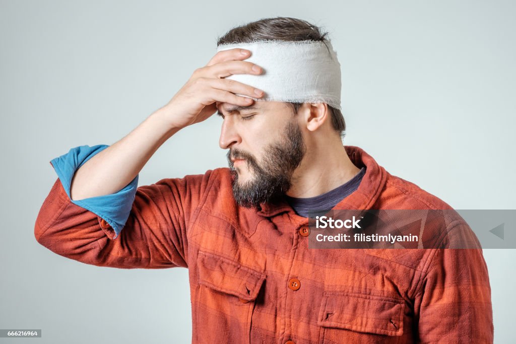 Portrait of man with bandages wrapped around his head isolated on gray background Shock Stock Photo