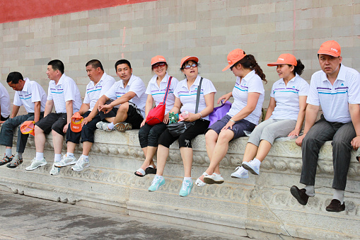 Asian tourists sitting and taking break on a low wall in Forbidden City, the Palace Museum, north of Tiananmen Square. Beijing, China, 18.june 2010