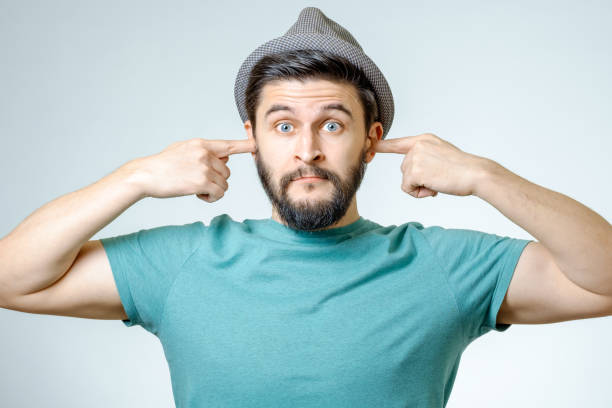 A portrait of a Caucasian adult male on a white background holding a magnifying glass to his ear to indicate that he is listening.