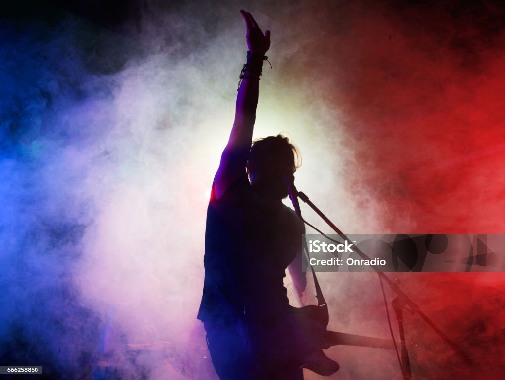 Silhouette of guitar player on stage. Silhouette of guitar player on stage. Dark background, smoke, spotlights Singer Stock Photo