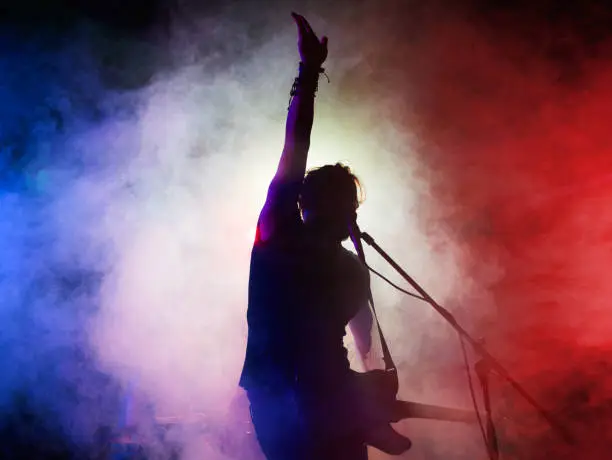 Silhouette of guitar player on stage. Dark background, smoke, spotlights