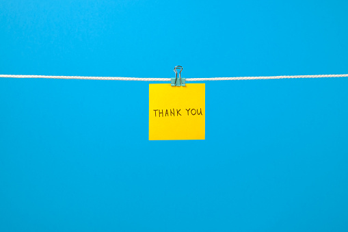 Yellow paper note on clothesline with text Thank You over colorful background