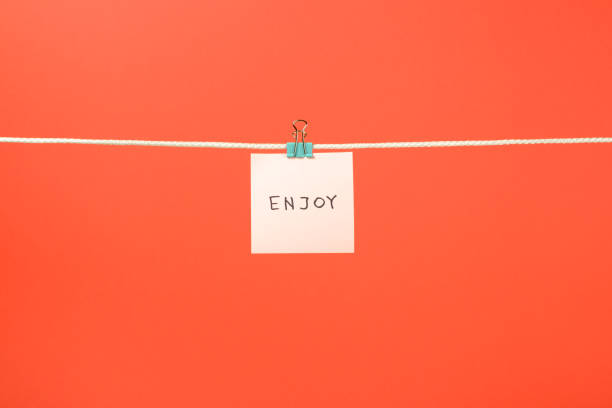 istock Pink paper note on clothesline with text Enjoy over colorful background 666265696