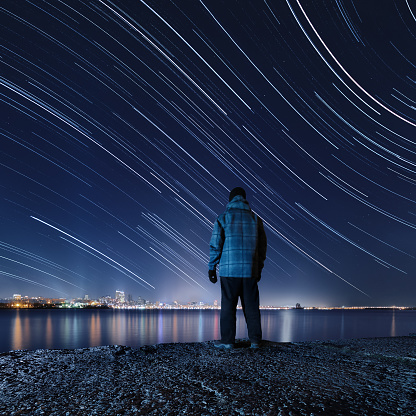 Hiker, standing on the river bank and enjoying a night view of the sky with a lot of stars and artificial lights of the city, Dnipropetrovsk