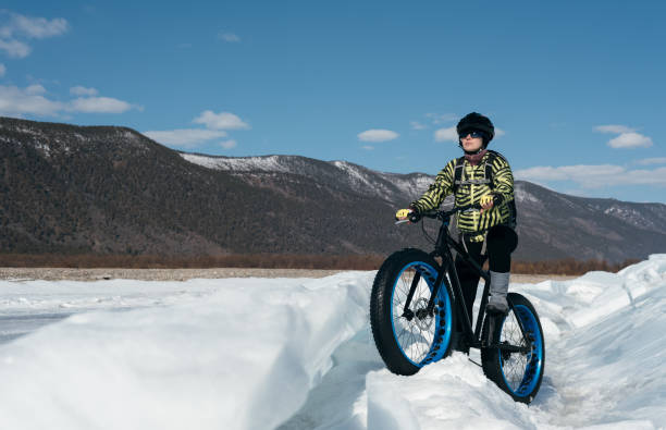 Fatbike (fat bike or fat-tire bike) Fatbike (also called fat bike or fat-tire bike) - Cycling on large wheels. Extreme girl riding a bike on snow melted ice. The Lake Baikal. cycling vest photos stock pictures, royalty-free photos & images