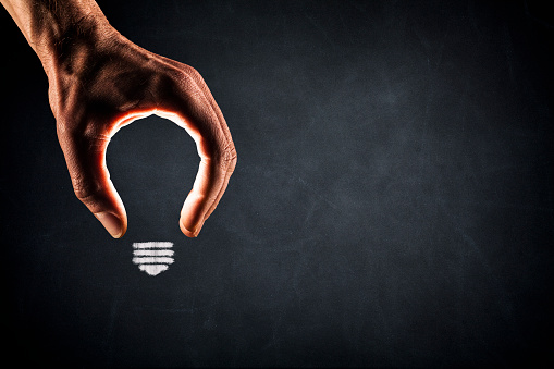 Photography of a hand forming a light bulb on a blackboard.