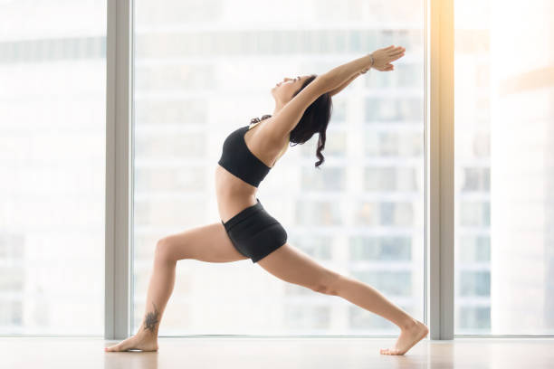 istock Young attractive woman in Warrior I pose against floor window 666305860