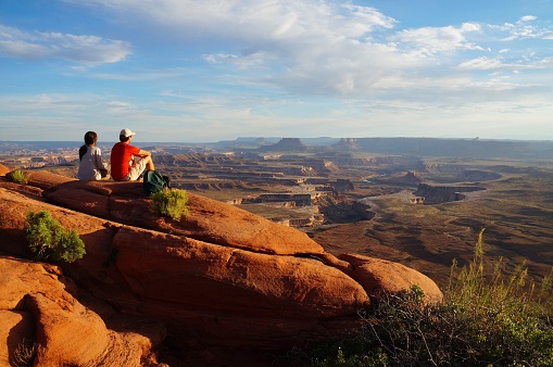 Couple sitting at the Green River Overview looking down into the valley carved by the Colorado and Green River. Canyonlands National Park, Utah, USA