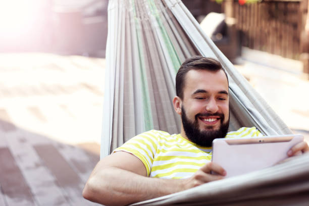 istock Picture showing happy man resting on hammock with tablet 666315428