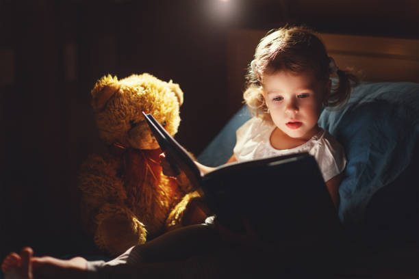 libro de lectura de chica de niño en la cama - child bedtime imagination dark fotografías e imágenes de stock
