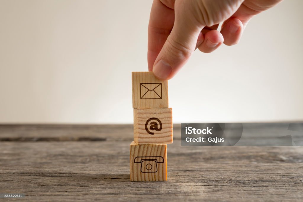 Contacts conceptual figure Hand placing little wooden cube on stack over table with email and phone pictograms, business contacts conceptual figure. Wood - Material Stock Photo