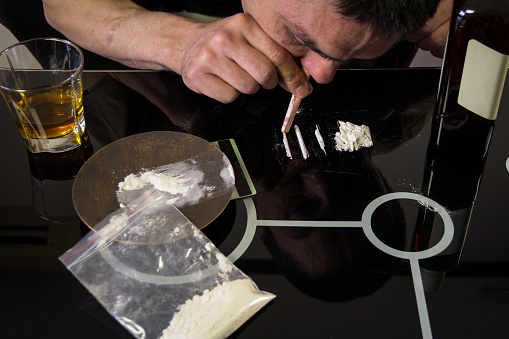 Junkie man snorting cocaine powder with rolled banknote