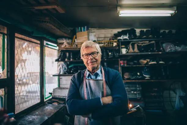 Photo of a senior man, owner of a cobbler's shop - proudly presents his workshop
