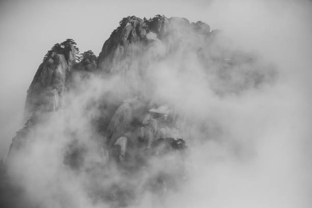 Dramatic black and white shooting from high point of morning mountains above grey mist, scenery hazy landscape of Thailand mountain peaks above clouds on moody day with rare plants and gas station