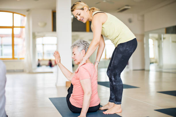 istruttore che aiuta la donna anziana a fare yoga - yoga class instructor yoga exercising foto e immagini stock