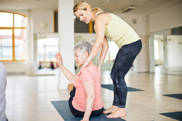 instruktor pomaga starszej kobiecie w robieniu jogi - yoga class instructor yoga exercising zdjęcia i obrazy z banku zdjęć