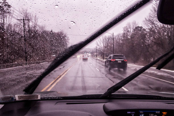 Car driver POV perspective - on an almost freezing 33 degrees Farenheit day - looking through the water splashed windshield between streaking windshield wipers while driving on a slippery, sloppy rural highway during a February winter rain and sleet storm near Rochester, NY in western New York State.