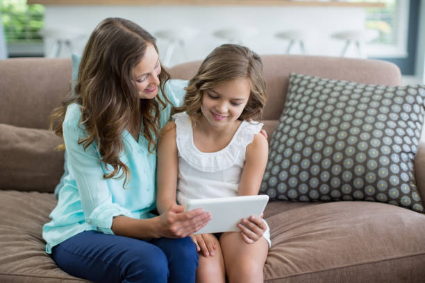 istock Smiling mother and daughter sitting on sofa using digital tablet in living room 666473140