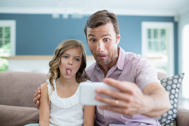 istock Father and daughter pulling funny faces while taking selfie in living room 666473440