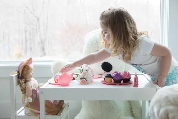 A little girl has a tea party with her doll and dog.