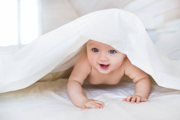 istock Pretty Infant crawls under a white cover in bed in bedroom 666517116