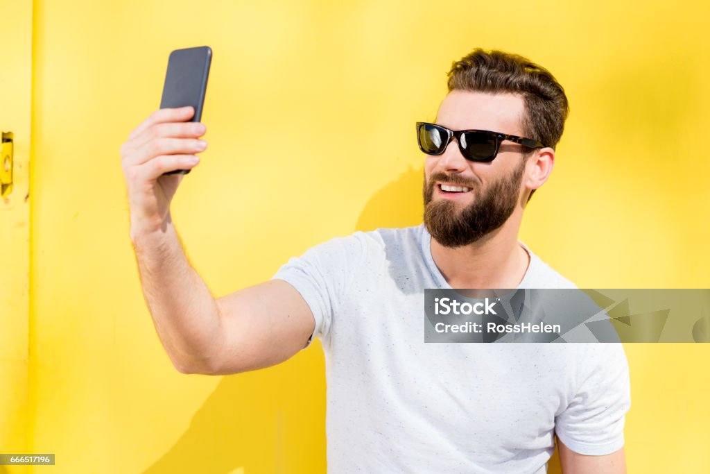 Portrait of a man on yellow background Colorful portrait of a handsome man dressed in white t-shirt on the yellow background Sunglasses Stock Photo