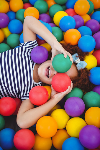 Cute smiling girl in sponge ball pool covering eyes with balls