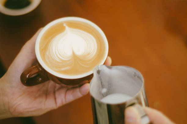 istock Cropped Hand Of Worker Pouring milk into Coffee Cup making Latte art pattern. 666540134