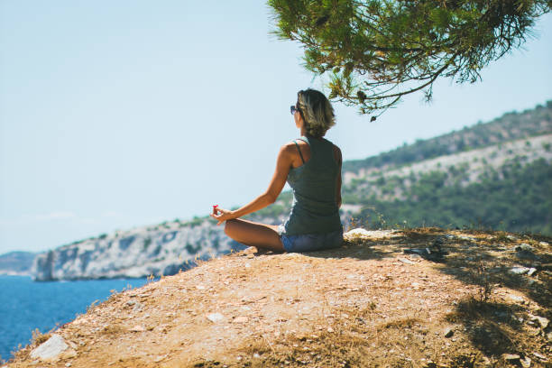 istock Young woman practicing yoga on a cliff, she meditating in lotus position. 666576622