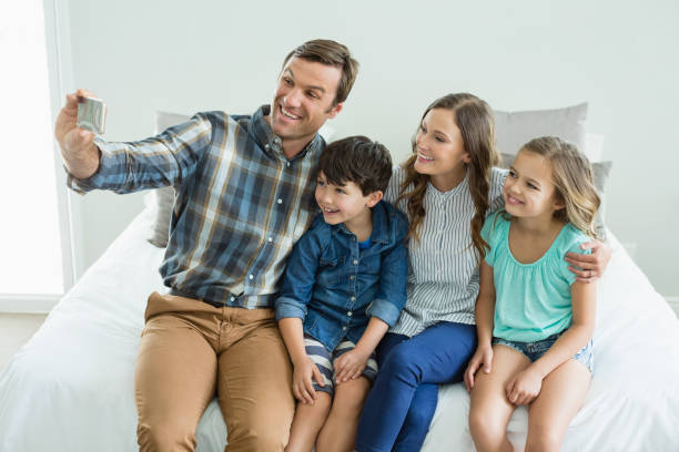 istock Smiling man taking selfie with family while sitting in bedroom 666614256