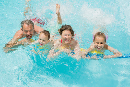 Portrait of happy parents and kids having fun in pool on a sunny day