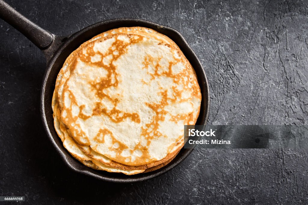 Crepes in cast iron pan Homemade crepes in cast iron pan over rustic black background with copy space - cooking fresh homemade breakfast crepes pancakes food Pancake Stock Photo