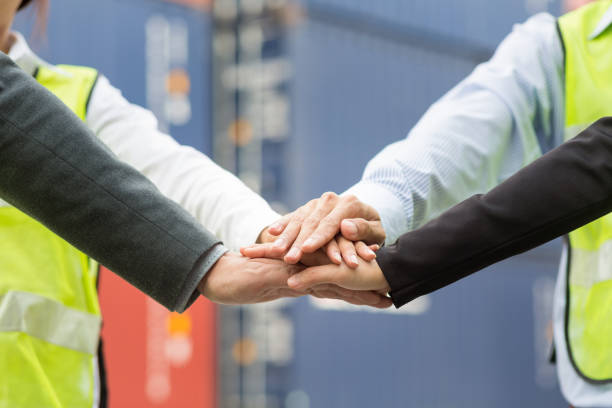 Business team in logistic industry join hand for collaboration after project achieve with container cargo for export and import in background. Teamwork concept