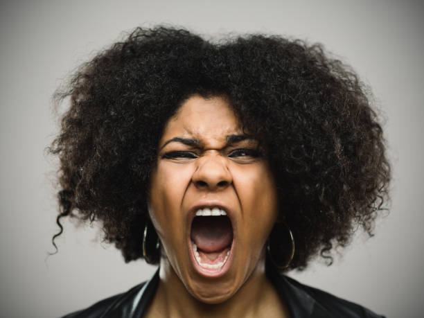 Close-up portrait of a shocked real young afro american woman Close-up portrait of shocked real young afro american woman screaming. Amazed female against gray background. Horizontal studio photography from a DSLR camera. Sharp focus on eyes. black woman screaming angry stock pictures, royalty-free photos & images