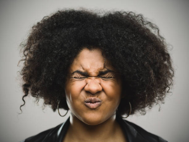 Close-up portrait of a stressed real young afro american woman Close-up portrait of stressed real young afro american woman clenching eyes. Shocked female against gray background. Horizontal frowning headshot close up studio shot stock pictures, royalty-free photos & images