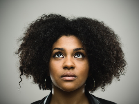 Close-up portrait of real young black woman looking up against gray background. Beautiful woman with curly hair. Studio photography from a DSLR camera. Sharp focus on eyes.