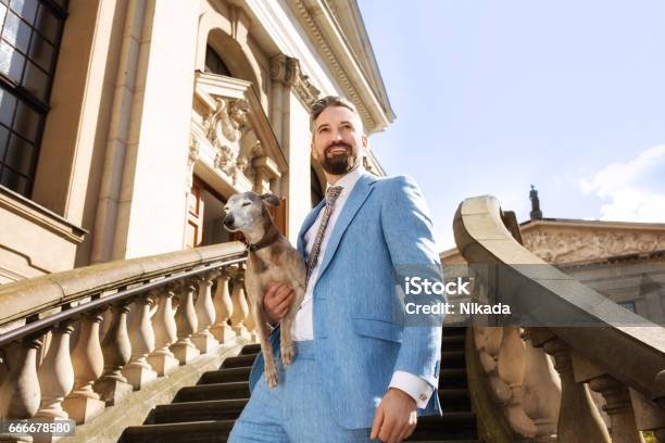 Low Angle View Of Thoughtful Businessman Carrying Dog On Steps Against Sky Stock Photo - Download Image Now