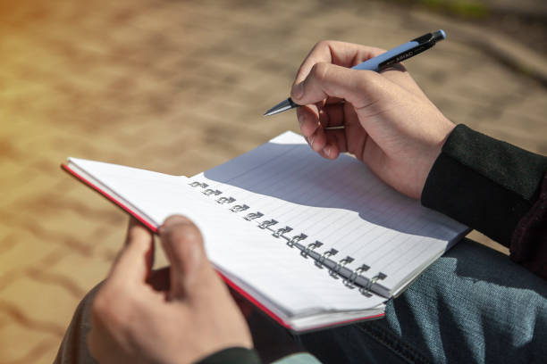 istock Man's hand writing on notebook, sketchbook outdoors 666691998