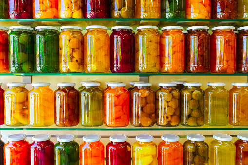 Various jars with Home Canning Fruits and Vegetables jam on glass shelves