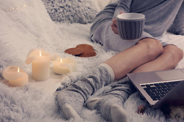 serata accogliente, calzini di lana caldi, coperta morbida, candele. donna che si rilassa a casa, beve cacao, usa il portatile. stile di vita confortevole. - bed human leg home interior comfortable foto e immagini stock