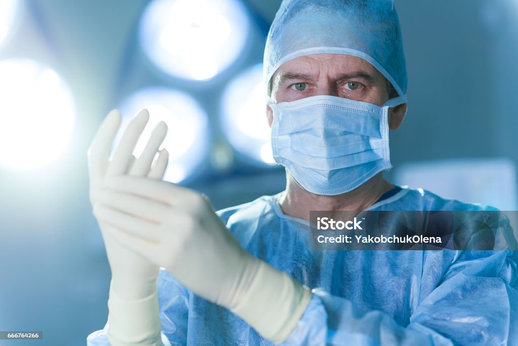 Serious male doctor dressed in special uniform Concentrated surgeon is wearing gloves and looking at camera with determination. Portrait Surgeon Stock Photo