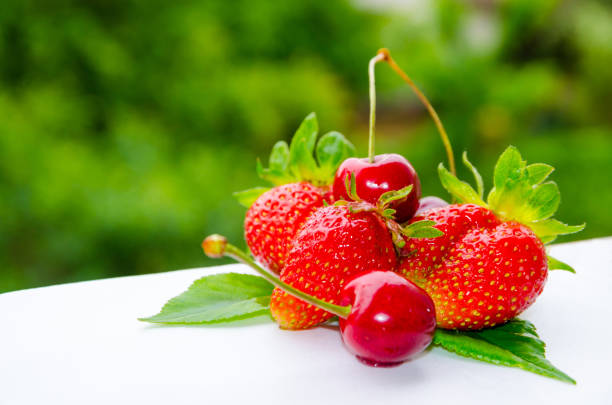 Fresh ripe strawberries and cherries on green trees background