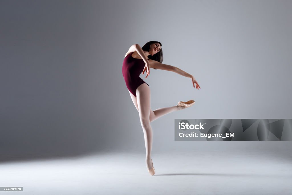 Young ballerina in a black dancing suit is posing on a grey background in the photostudio Slim ballerina is dancing in the white studio in the contrast light Ballet Stock Photo