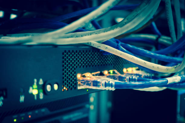 istock Close up of  network internet cables, patch cords connected to black switch router in data center glowing in the dark and cold tone 666795714